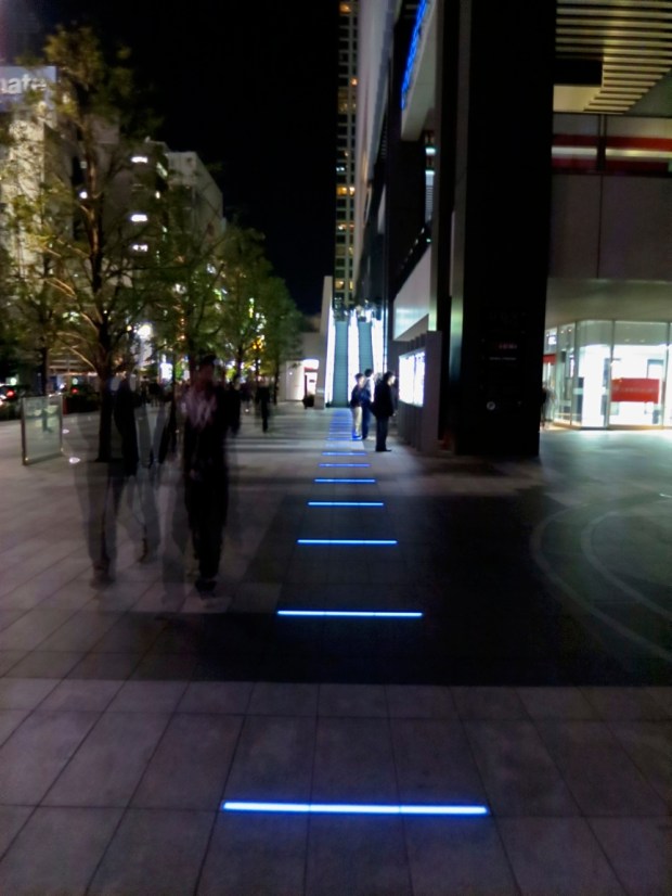 On the corner near the UDX building, a mysterious path of blue neon bars leads up up the stairs to the Anime Center, and beyond.